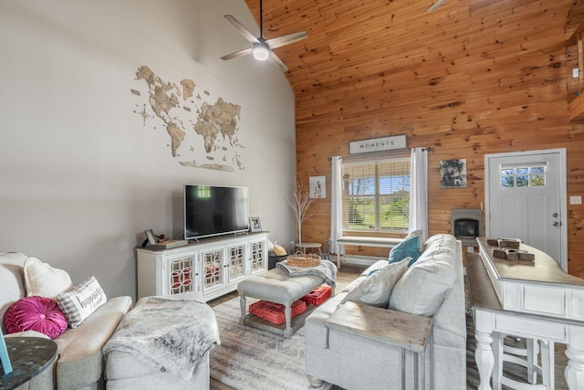 living room with wooden walls, ceiling fan, a wood stove, and high vaulted ceiling