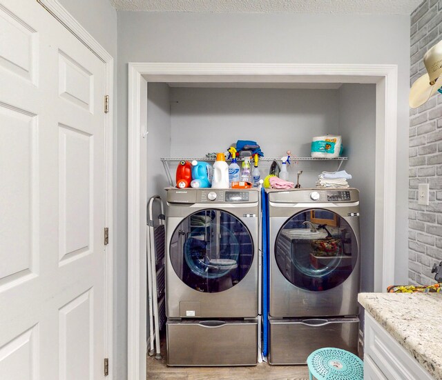 laundry room with separate washer and dryer, a textured ceiling, brick wall, and light hardwood / wood-style flooring