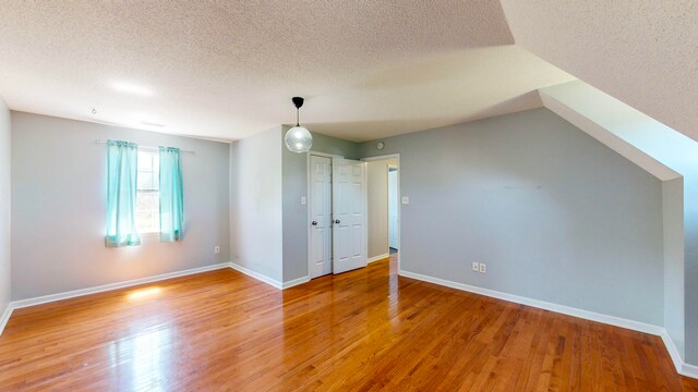 additional living space featuring a textured ceiling, hardwood / wood-style floors, and lofted ceiling