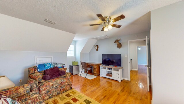 living room with ceiling fan, light hardwood / wood-style floors, a textured ceiling, and vaulted ceiling