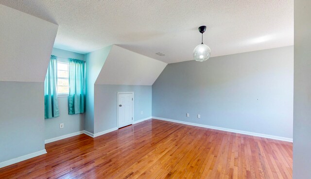 additional living space featuring lofted ceiling, a textured ceiling, and light wood-type flooring