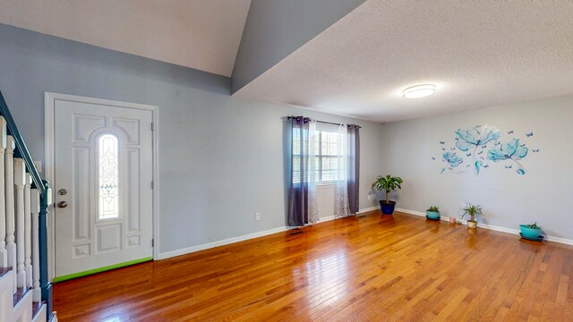 foyer featuring vaulted ceiling, wood-type flooring, and a textured ceiling