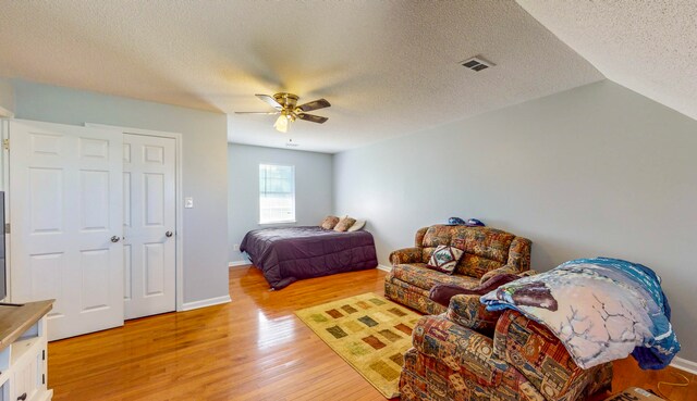 bedroom featuring vaulted ceiling, ceiling fan, light hardwood / wood-style floors, and a textured ceiling