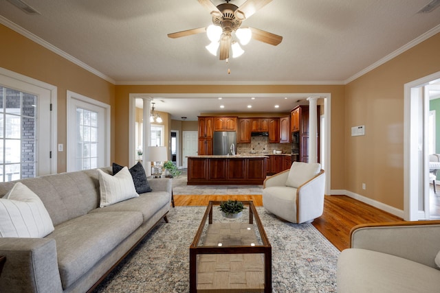 living room with ceiling fan with notable chandelier, light hardwood / wood-style floors, and crown molding