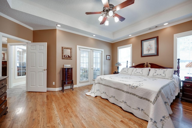 bedroom with ceiling fan, a raised ceiling, light hardwood / wood-style flooring, crown molding, and multiple windows