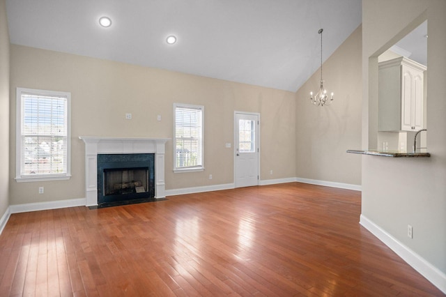 unfurnished living room featuring light wood-style flooring, baseboards, vaulted ceiling, and a high end fireplace