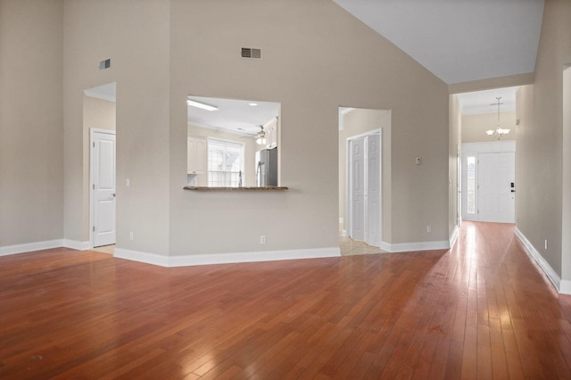 unfurnished living room with light wood-style floors, baseboards, visible vents, and high vaulted ceiling