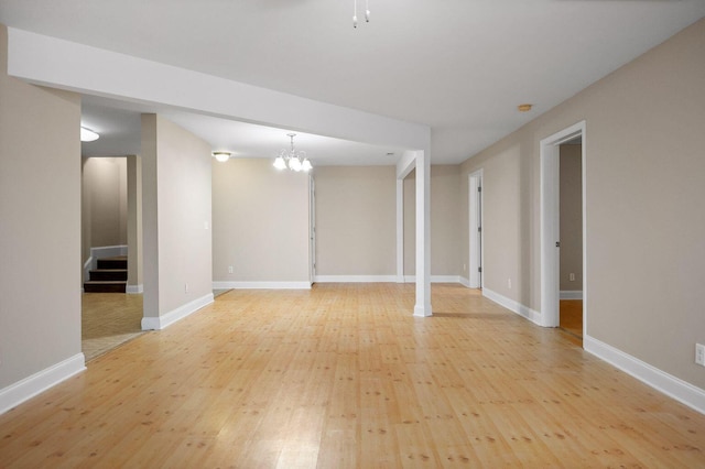 unfurnished room with a notable chandelier, stairway, light wood-type flooring, and baseboards