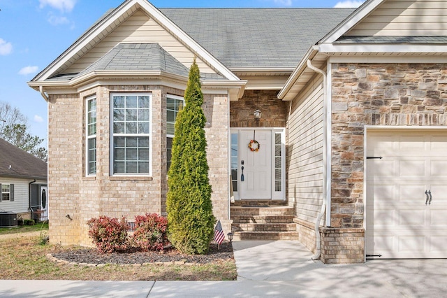 entrance to property featuring a garage, stone siding, central AC unit, and brick siding