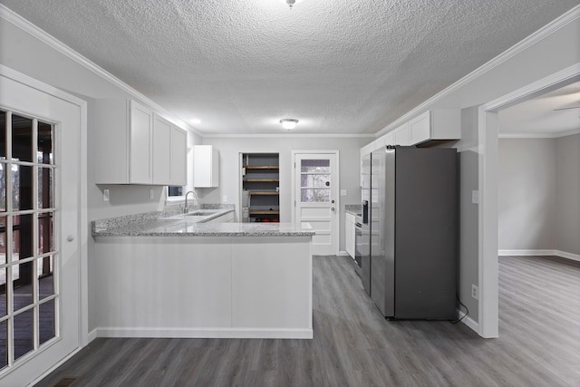 kitchen featuring white cabinetry, crown molding, wood-type flooring, stainless steel fridge, and kitchen peninsula