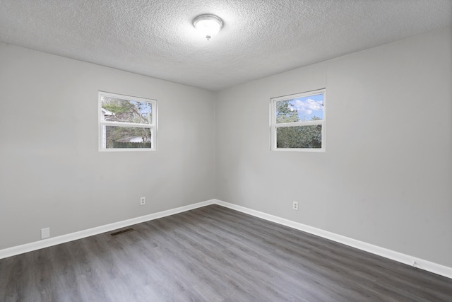 empty room with a healthy amount of sunlight, a textured ceiling, and dark hardwood / wood-style floors