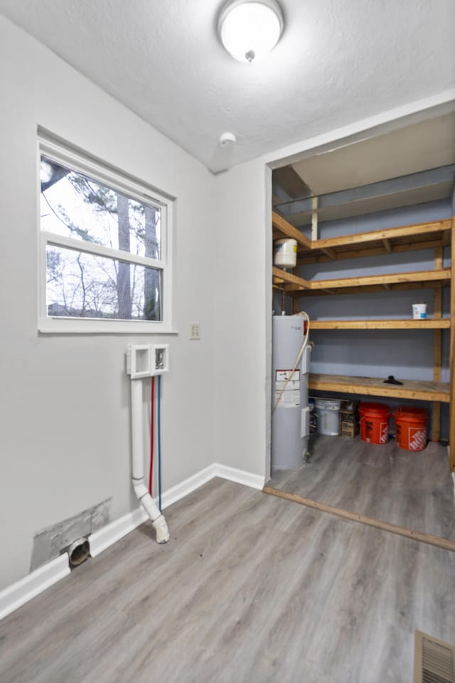 laundry room featuring wood-type flooring, electric water heater, and a textured ceiling