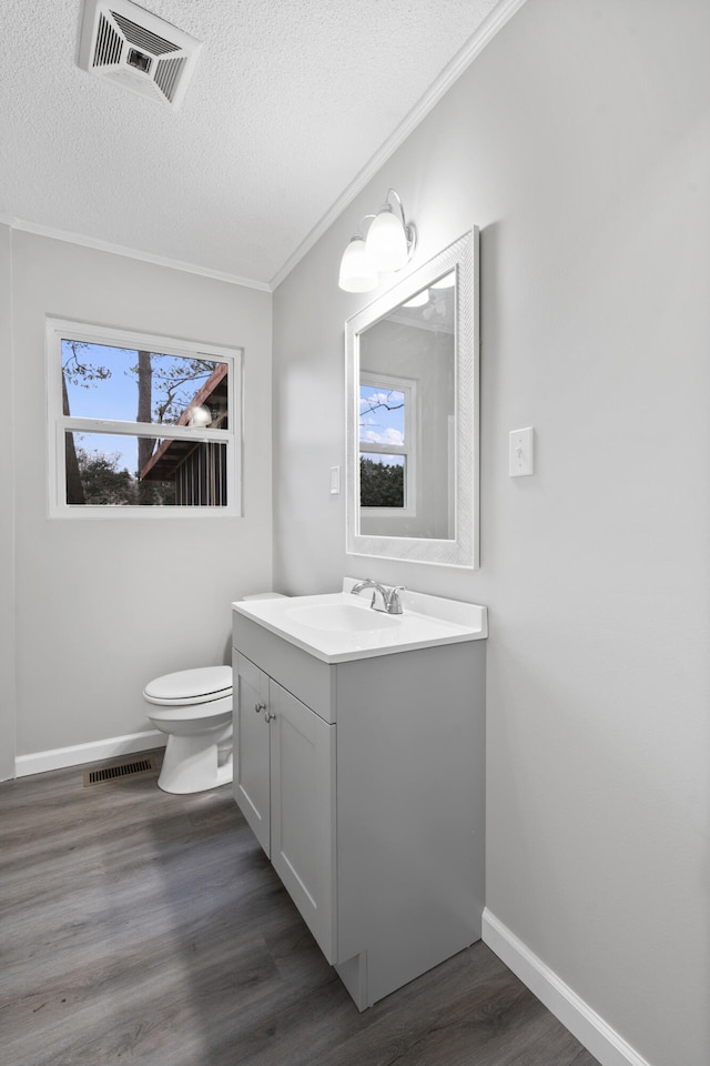 bathroom with toilet, a textured ceiling, ornamental molding, vanity, and hardwood / wood-style flooring