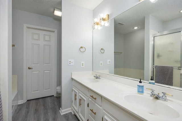 bathroom with a textured ceiling, wood finished floors, a sink, and a shower with shower door