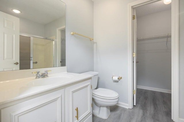 bathroom with a stall shower, toilet, wood finished floors, a spacious closet, and vanity