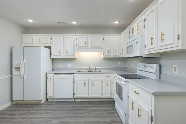 kitchen featuring white appliances, wood finished floors, a sink, white cabinetry, and light countertops