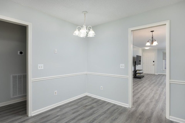 unfurnished room with a textured ceiling, a notable chandelier, wood finished floors, visible vents, and baseboards