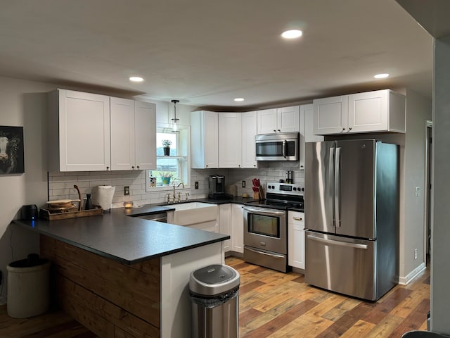 kitchen with white cabinets, appliances with stainless steel finishes, light hardwood / wood-style flooring, and hanging light fixtures