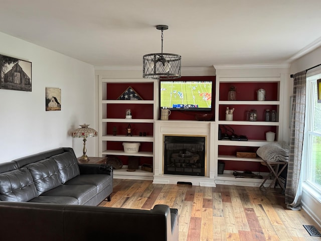 living room with hardwood / wood-style floors, crown molding, a wealth of natural light, and a chandelier