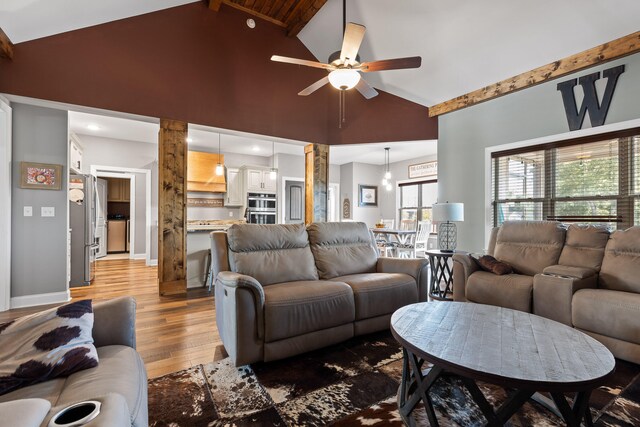 living room with beam ceiling, light wood-type flooring, high vaulted ceiling, and ceiling fan