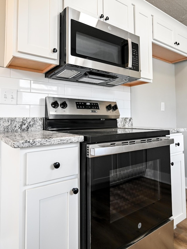 kitchen with appliances with stainless steel finishes, dark hardwood / wood-style floors, white cabinets, backsplash, and light stone countertops