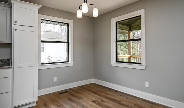 unfurnished room with a healthy amount of sunlight, a chandelier, and dark hardwood / wood-style flooring