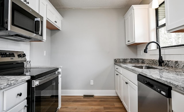 kitchen featuring sink, white cabinets, backsplash, stainless steel appliances, and light stone countertops