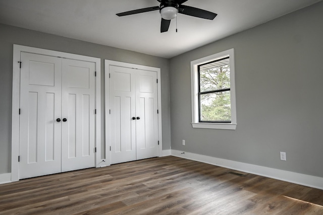 unfurnished bedroom with dark hardwood / wood-style flooring, ceiling fan, and multiple closets