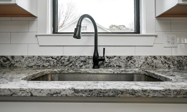 details featuring light stone countertops, sink, white cabinets, and backsplash