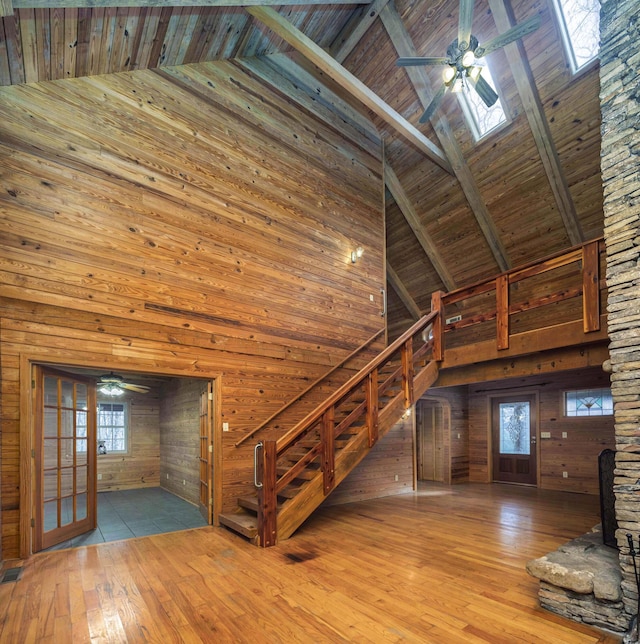 unfurnished living room with high vaulted ceiling, wooden walls, a skylight, light wood-type flooring, and wood ceiling