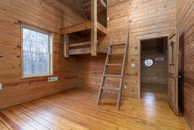 unfurnished bedroom with light wood-type flooring, wooden walls, and vaulted ceiling