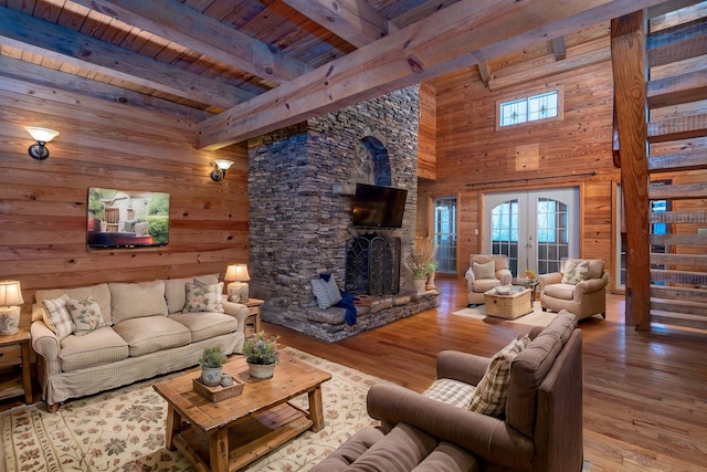 living room featuring french doors, a stone fireplace, beam ceiling, wood-type flooring, and wood ceiling