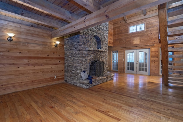 unfurnished living room with french doors, a stone fireplace, beamed ceiling, wood ceiling, and hardwood / wood-style flooring