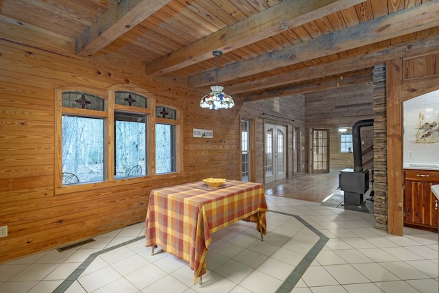 dining room with light tile patterned floors, a wood stove, beam ceiling, and wood walls