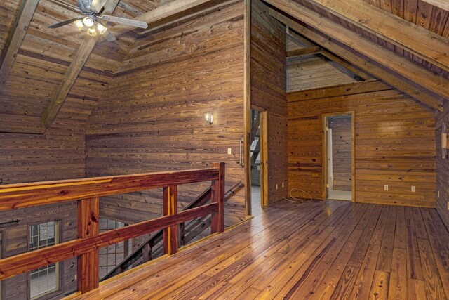 additional living space featuring ceiling fan, lofted ceiling with beams, hardwood / wood-style flooring, wooden ceiling, and wood walls