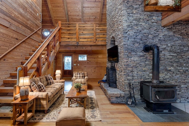 unfurnished living room with beam ceiling, a wood stove, light hardwood / wood-style flooring, a towering ceiling, and wood ceiling