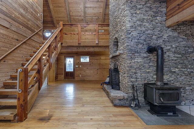 unfurnished living room featuring wood ceiling, light hardwood / wood-style flooring, beamed ceiling, a high ceiling, and wood walls