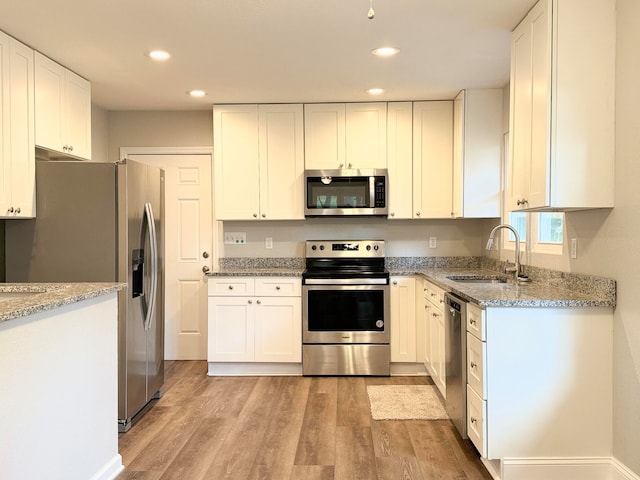 kitchen with sink, light stone counters, appliances with stainless steel finishes, white cabinets, and light wood-type flooring