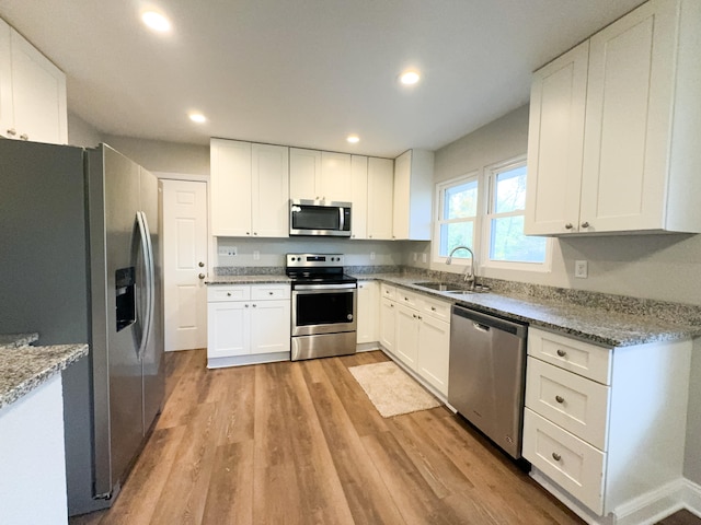 kitchen featuring white cabinets, sink, light stone countertops, light hardwood / wood-style floors, and stainless steel appliances