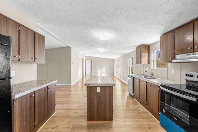 kitchen featuring sink, light wood-type flooring, a textured ceiling, appliances with stainless steel finishes, and a kitchen island