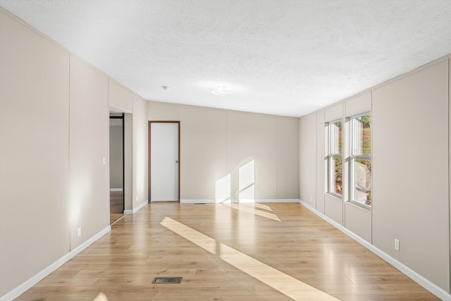 unfurnished room featuring light wood-type flooring, a textured ceiling, and vaulted ceiling
