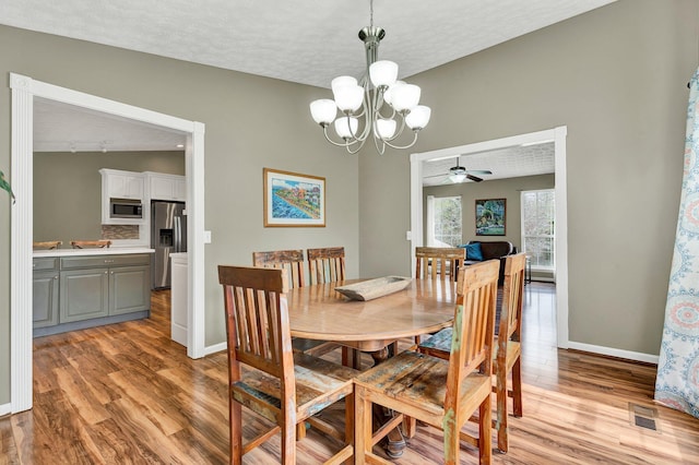 dining space with ceiling fan with notable chandelier, baseboards, light wood-style floors, and a textured ceiling
