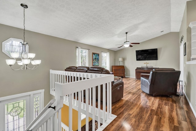 interior space featuring baseboards, a textured ceiling, wood finished floors, ceiling fan with notable chandelier, and lofted ceiling