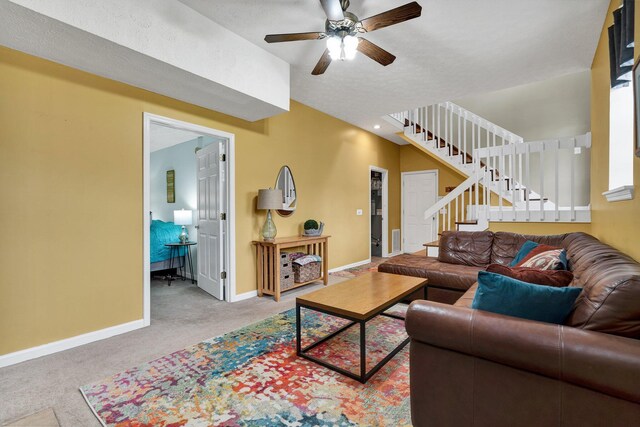 carpeted living area featuring baseboards, stairway, and ceiling fan