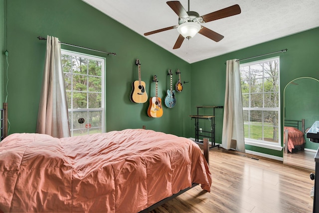 bedroom with ceiling fan, multiple windows, wood finished floors, and vaulted ceiling