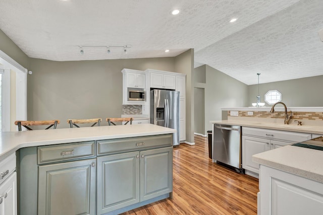 kitchen with light countertops, white cabinets, lofted ceiling, stainless steel appliances, and a sink