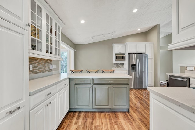 kitchen with light countertops, appliances with stainless steel finishes, a peninsula, light wood-style flooring, and lofted ceiling