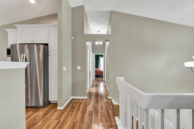 corridor featuring an inviting chandelier, a textured ceiling, lofted ceiling, light wood finished floors, and baseboards