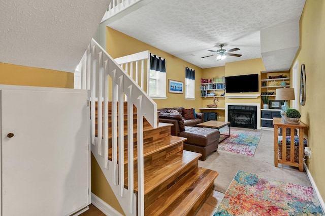 living room featuring baseboards, a fireplace, stairway, a textured ceiling, and ceiling fan