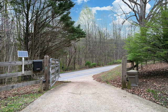 view of road featuring a forest view and a gate